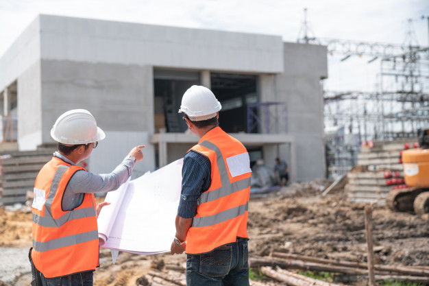 Profesionales graduados en construcción y mantenimiento de CBT College revisan planos frente a obra.