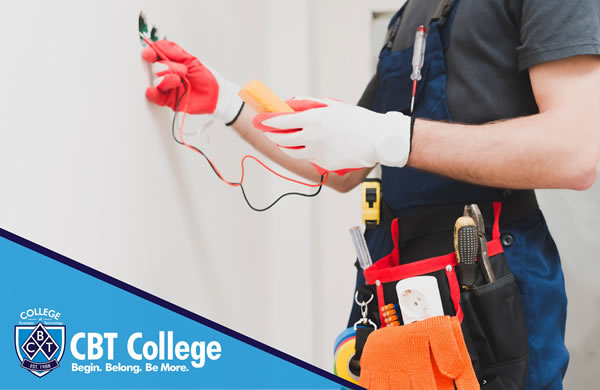 Electricista capacitado en CBT College trabaja con cables de tablero eléctrico con guantes y herramientas en cinturón.