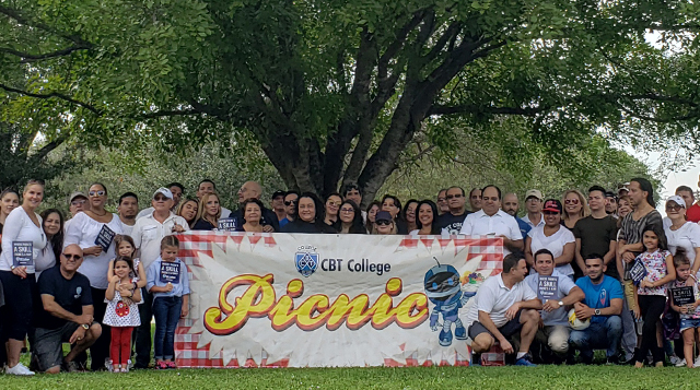 Estudiante de curso técnico diploma en electricidad en Campus de Hialeah de CBT Technology Institute sonríe frente a cartel con logo.